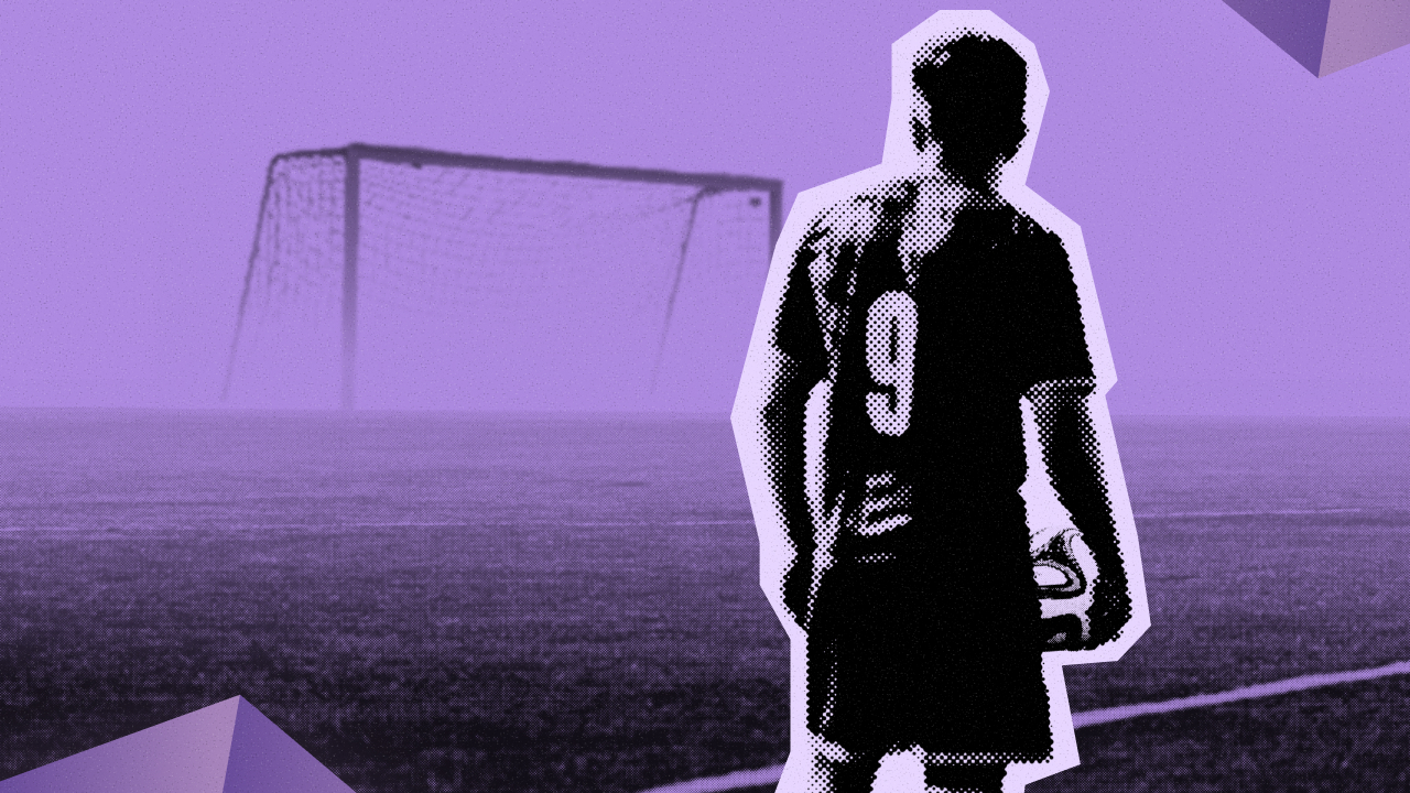 A footballer standing on a pitch holding a ball, back to the camera, facing an empty goal in the mist.