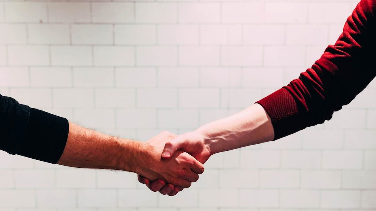 A close-up of two people shaking hands in agreement against a tiled wall background.