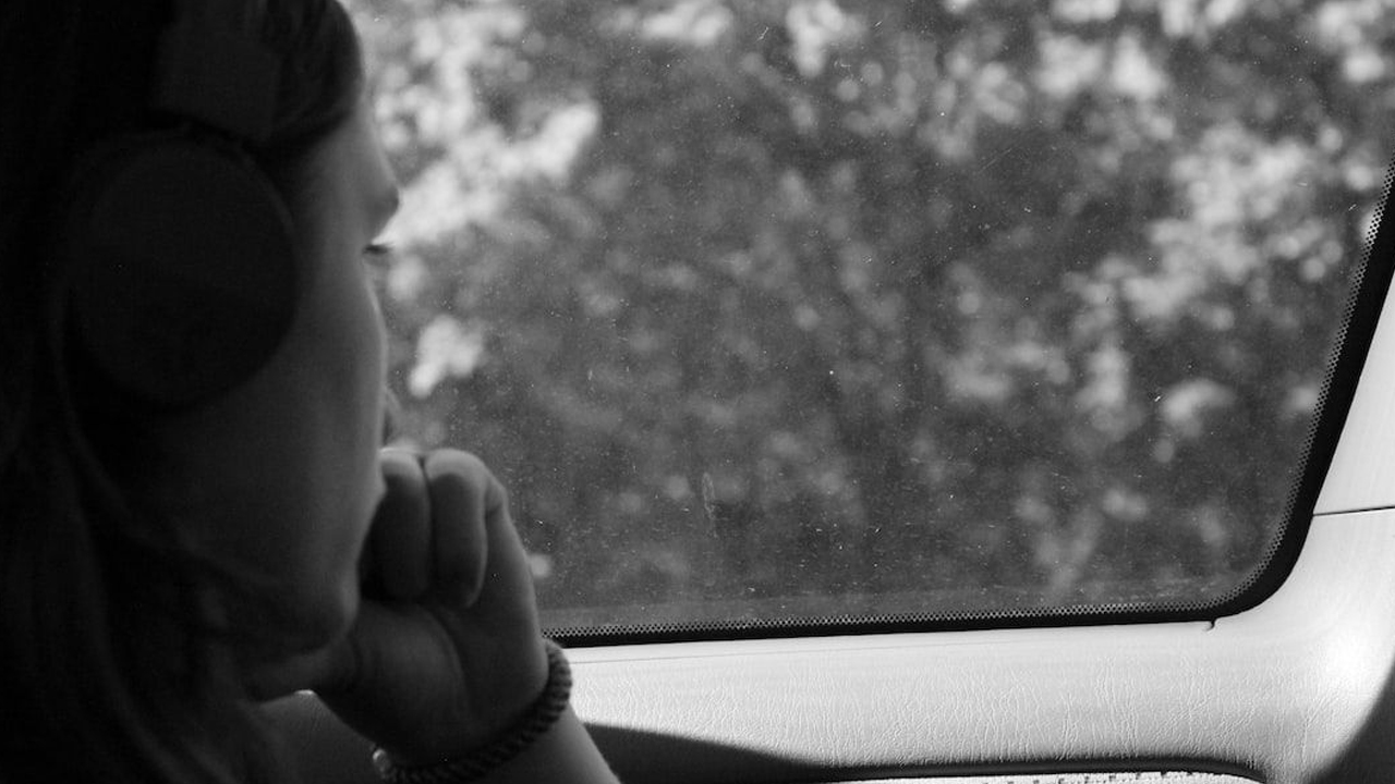 A person wearing headphones gazing out of a car window in thoughtful silence, captured in black and white.
