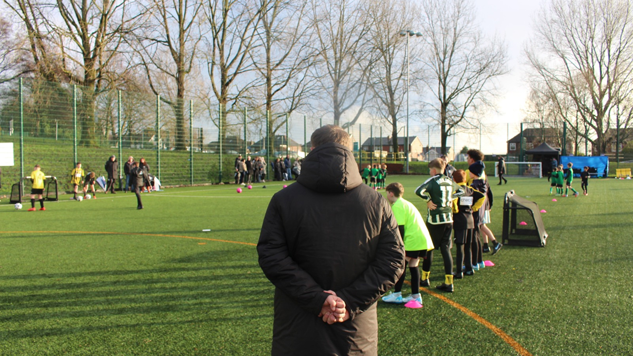 A grassroots football coach observing children training on the 3G pitch during the Grassroots Coachathon community event.