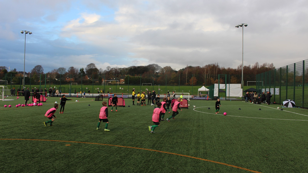 Young grassroots football players in pink bibs training during the Grassroots Coachathon on an outdoor 3G pitch.