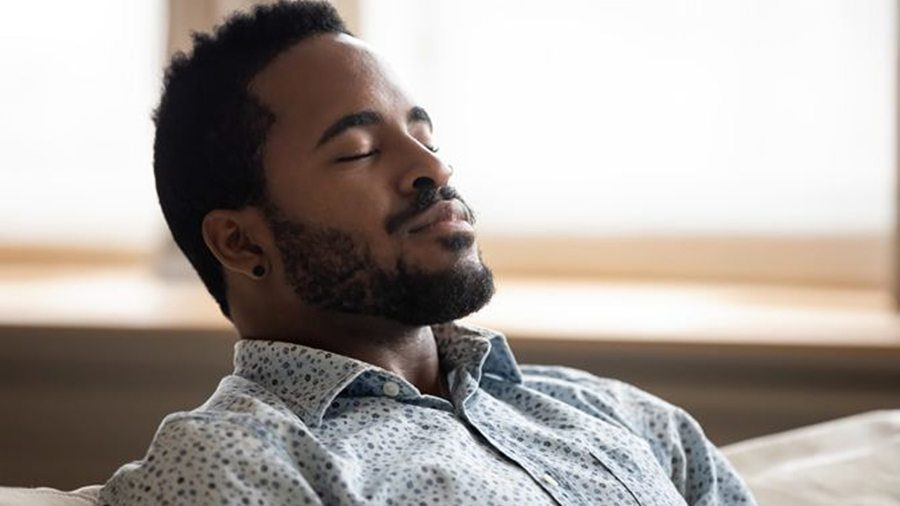 Calm man with eyes closed practicing deep breathing while sitting indoors